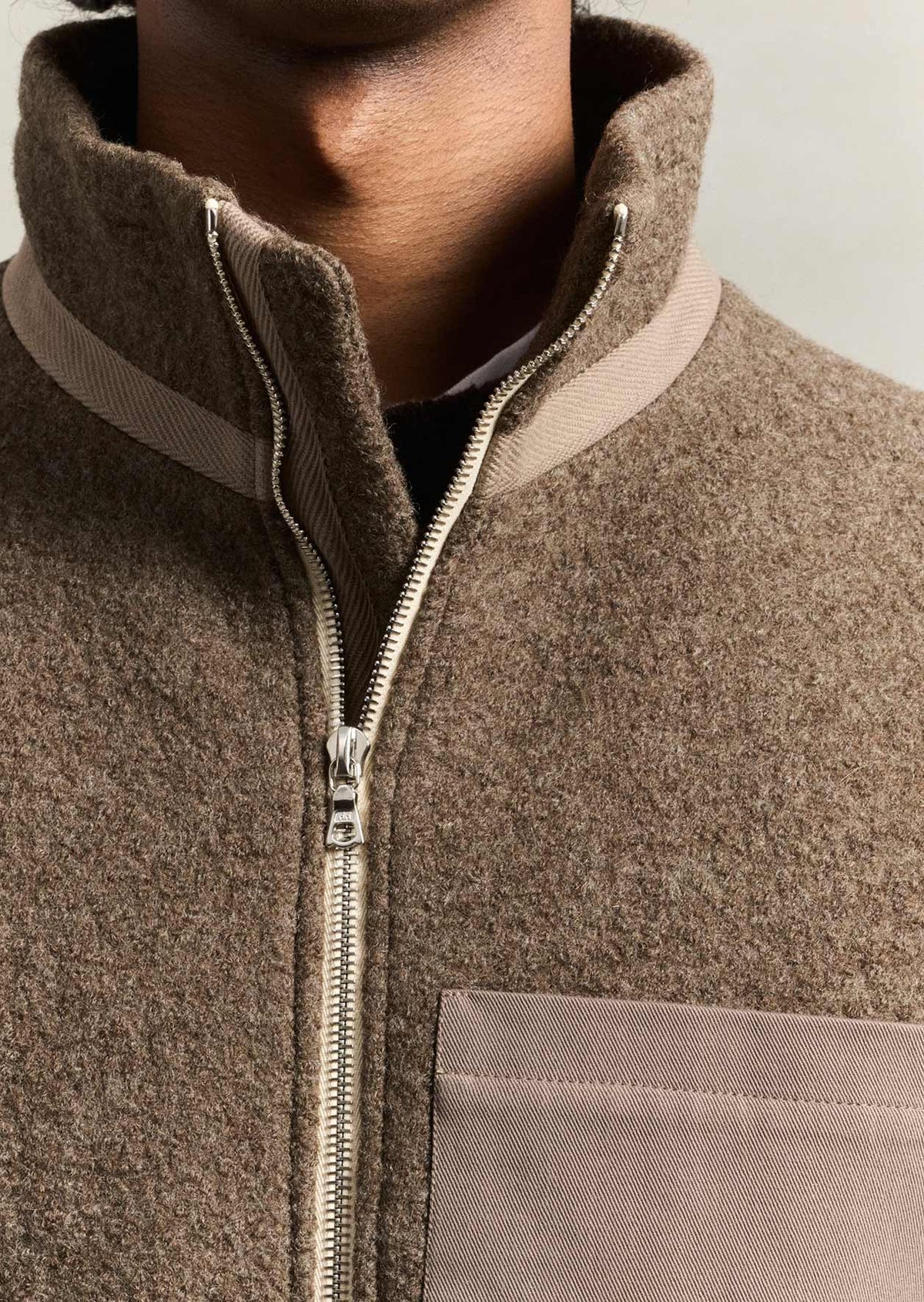 Close-up of model wearing the De Bonne Facture Boiled Wool Bookstore Jacket in Ash Brown showing the front zip, high collar and chest pocket.