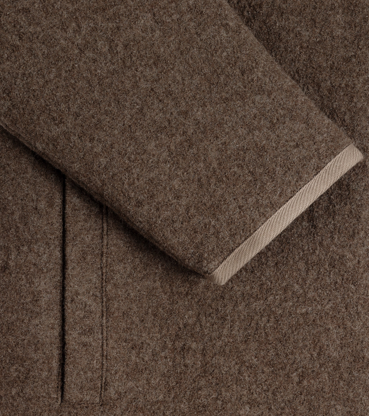 Close-up of the De Bonne Facture Boiled Wool Bookstore Jacket in Ash Brown showing the cuff with a contrasting light beige trim and side welt pocket.