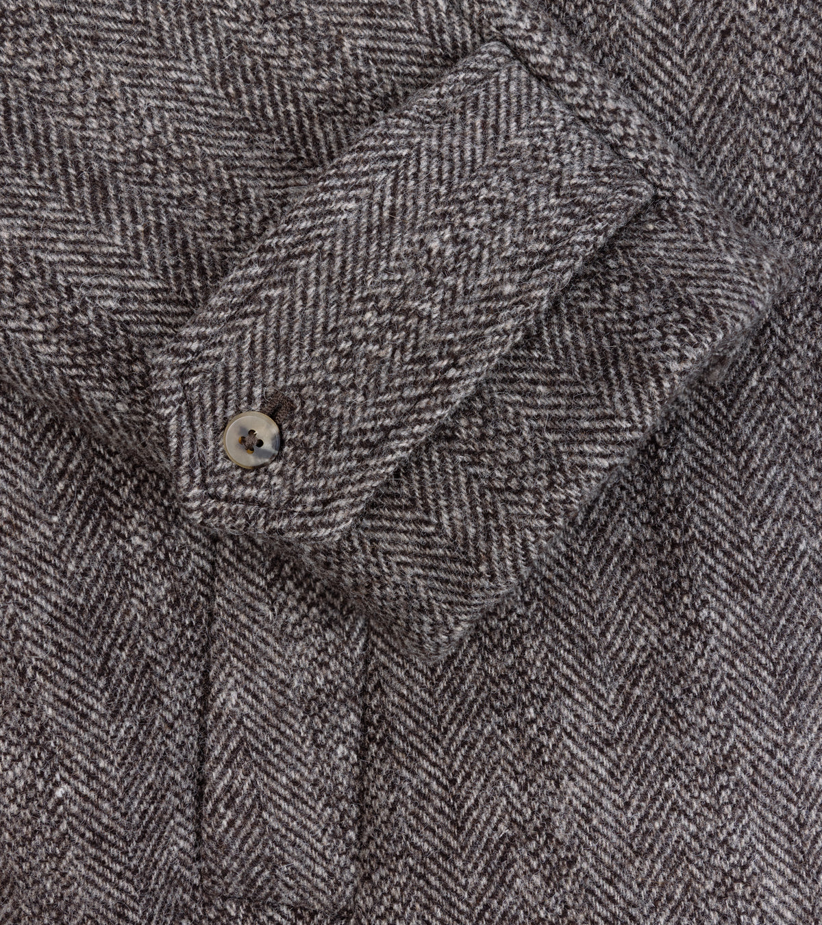 Close-up of the De Bonne Facture Herringbone Wool Overcoat in Undyed Brown, showing a buttoned cuff and pocket detail.