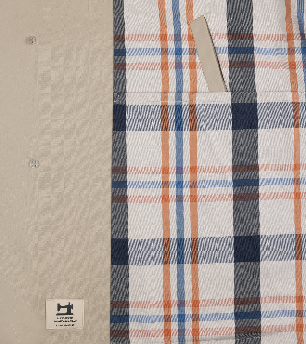 Close-up detail of the navy, orange and cream plaid pattern lining of the Sanyo 100 Year Lightweight Gabardine Balmacaan Coat in Beige. Also show is the inside pocket.