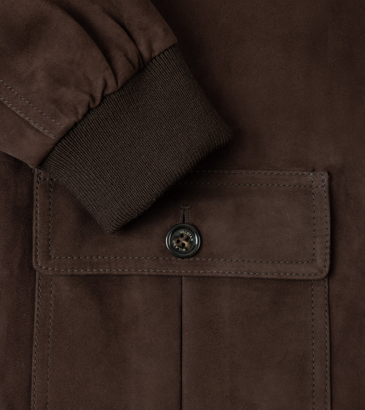 Close-up of a dark brown suede jacket featuring a ribbed knit cuff and a buttoned flap pocket.