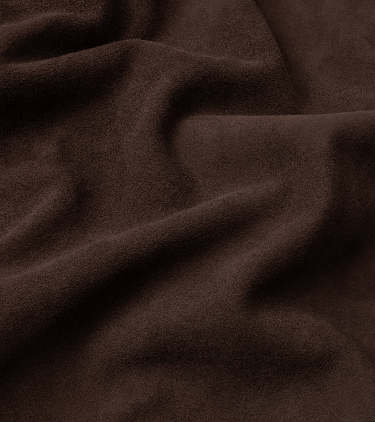 A close-up of draped dark brown suede or microfiber fabric with soft folds and a matte texture.