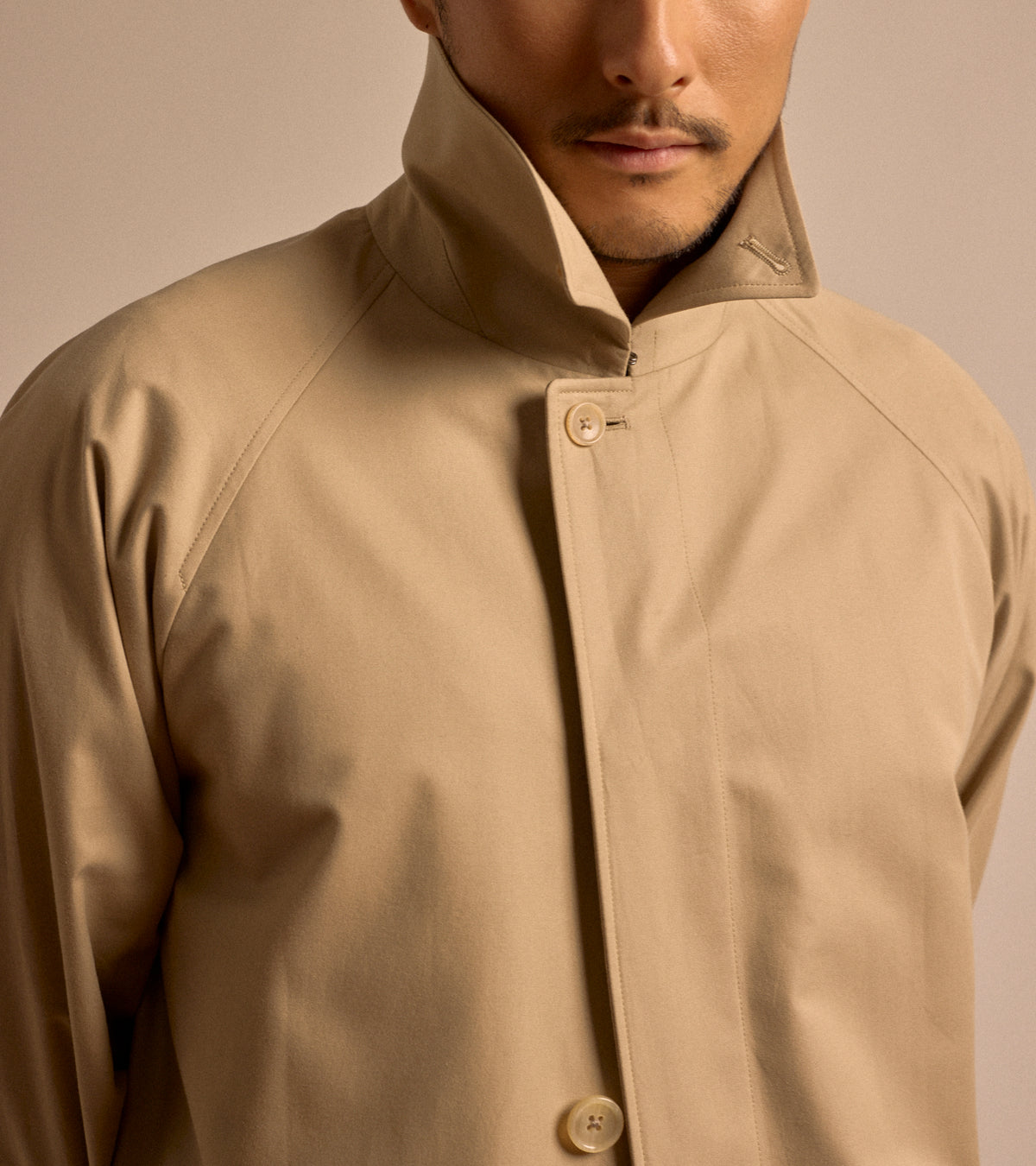 Close-up detailed shot of the model wearing the Sanyo 100 Year Lightweight Gabardine Balmacaan Coat in Beige.