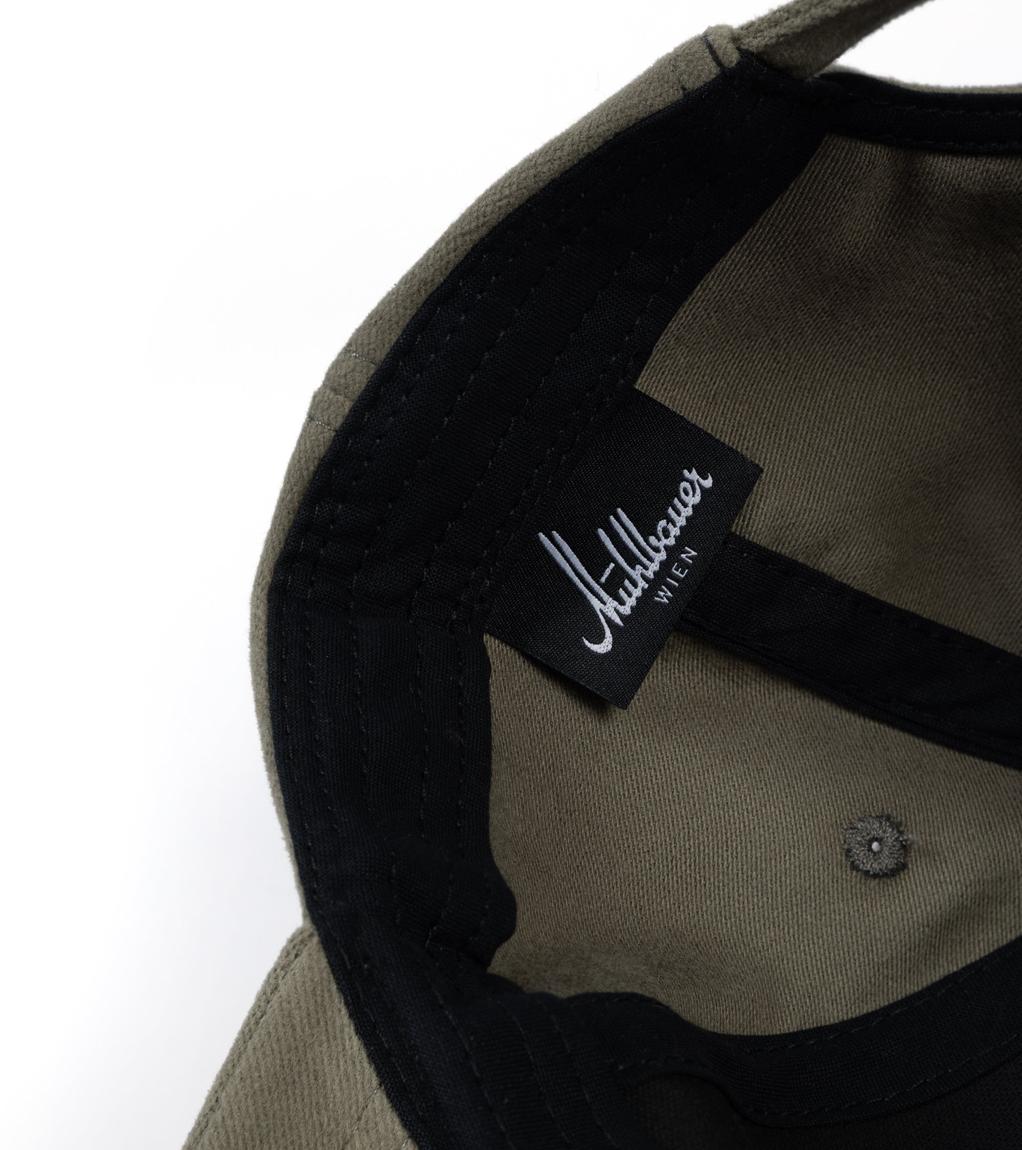 Close-up of the interior of a structured cap, showing an olive green fabric crown with black trim, a black fabric label stitched.