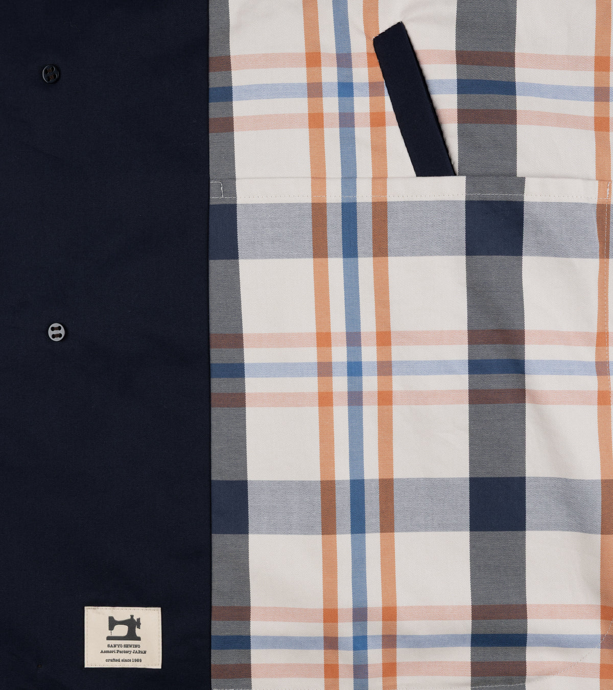 Close-up detail of the navy, orange and cream plaid pattern lining of the Sanyo 100 Year Lightweight Gabardine Balmacaan Coat in Navy. Also show is the inside pocket.