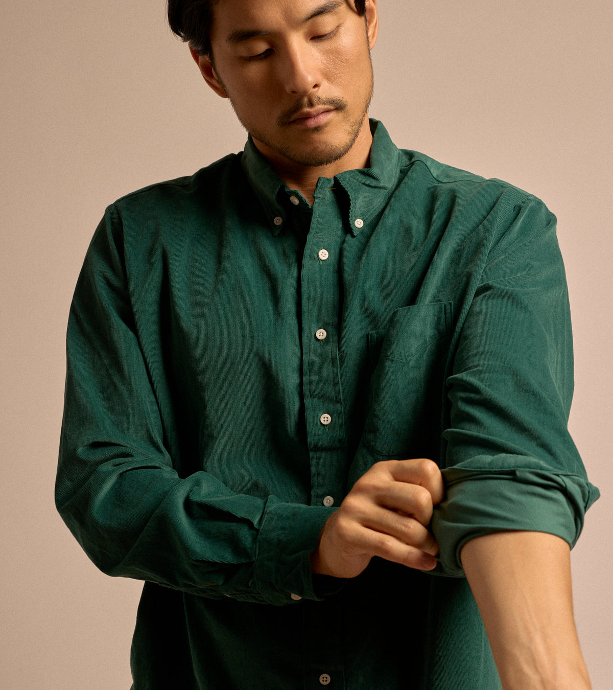 Model wearing the Gitman Vintage Fine Cord Button Down Shirt in Green. Front view, model rolling up his left sleeve.