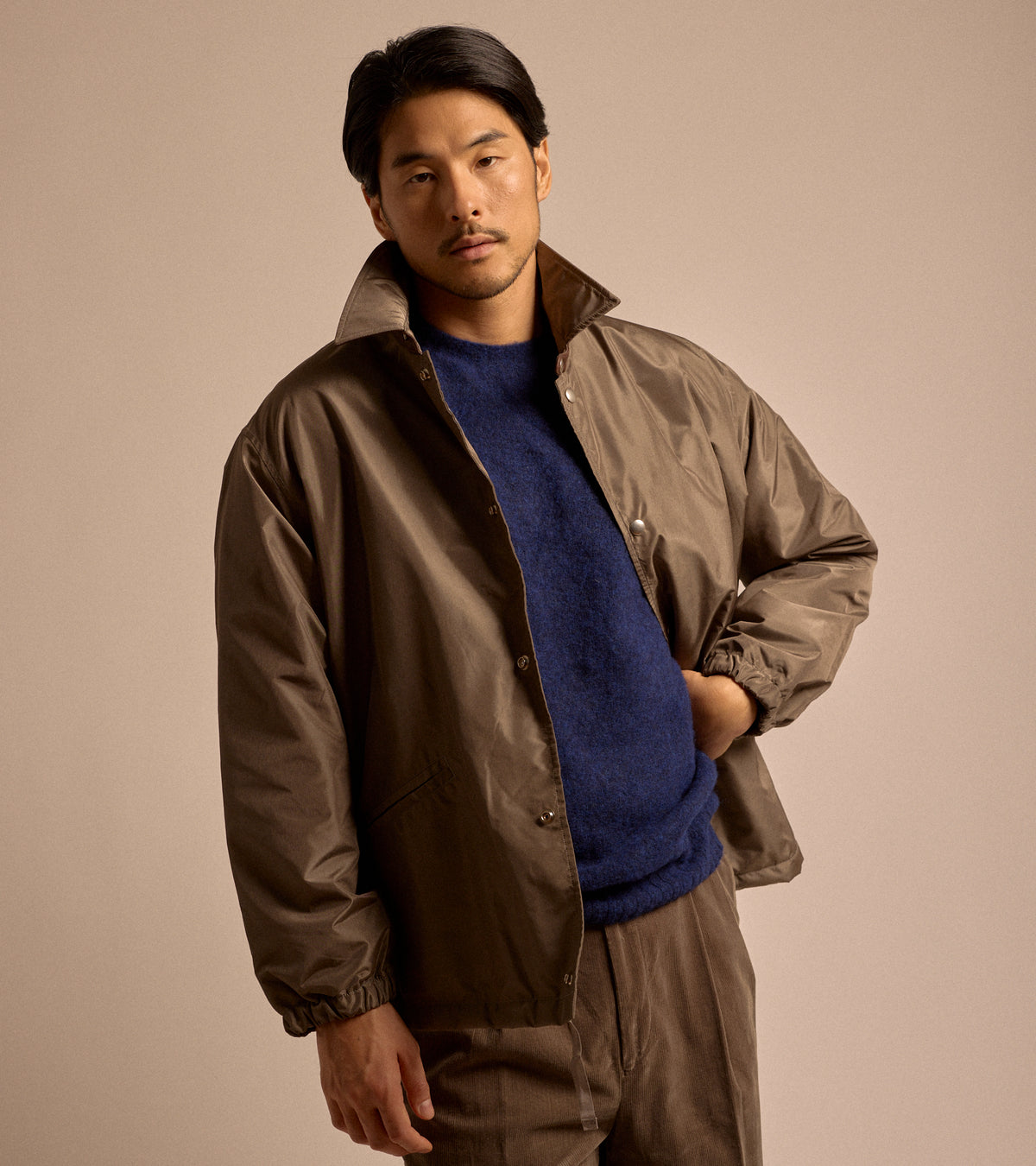 Model wearing Kaptain Sunshine Silk Poly Coach Jacket: Stone Grey. Front view, styled with a Navy lambswool sweater brown corduroy trousers.