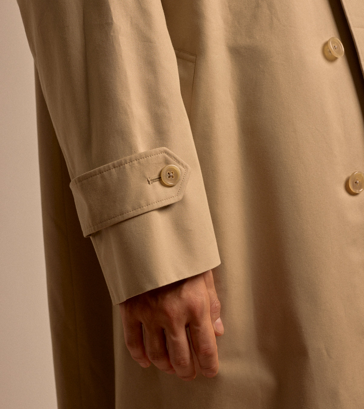Model wearing the Sanyo 100 Year Lightweight Gabardine Balmacaan Coat in Beige. Close-up detailed shot of the sleeve and fabric.